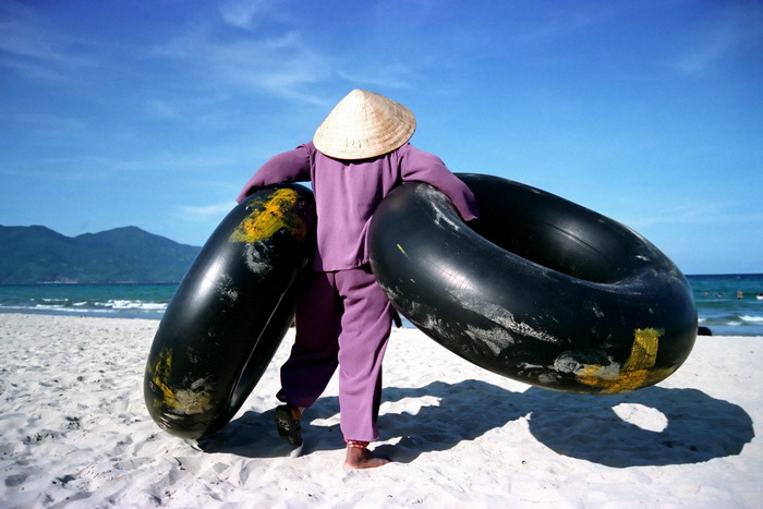 An elderly woman carries inflated tractor tyres on China Beach in Vietnam